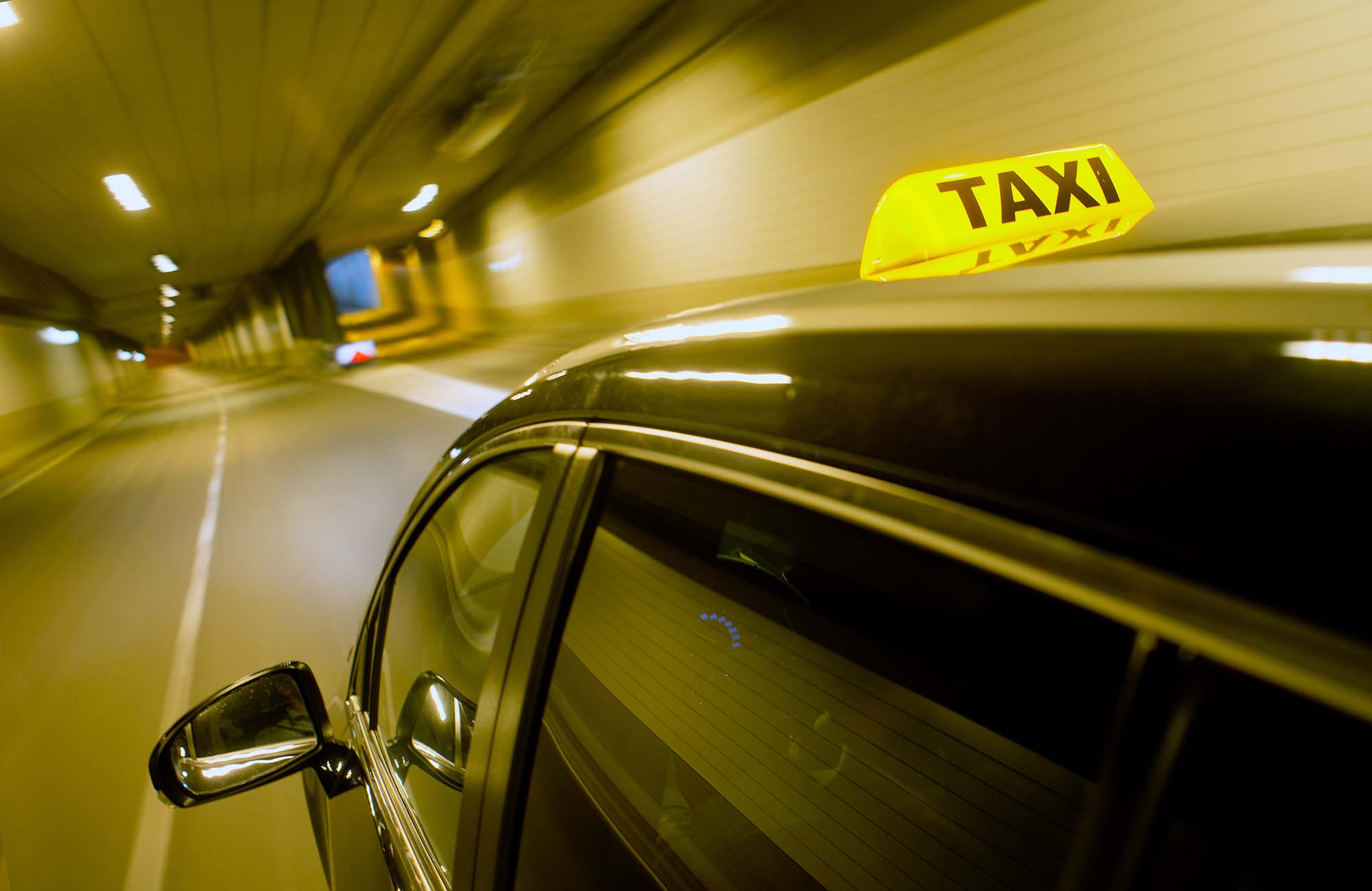 A black taxi, driving through a dunnel, with the taxi sign lit, apporaching a junction and exit ramp