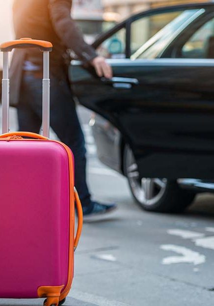 Pink suitcase beside black car at airport